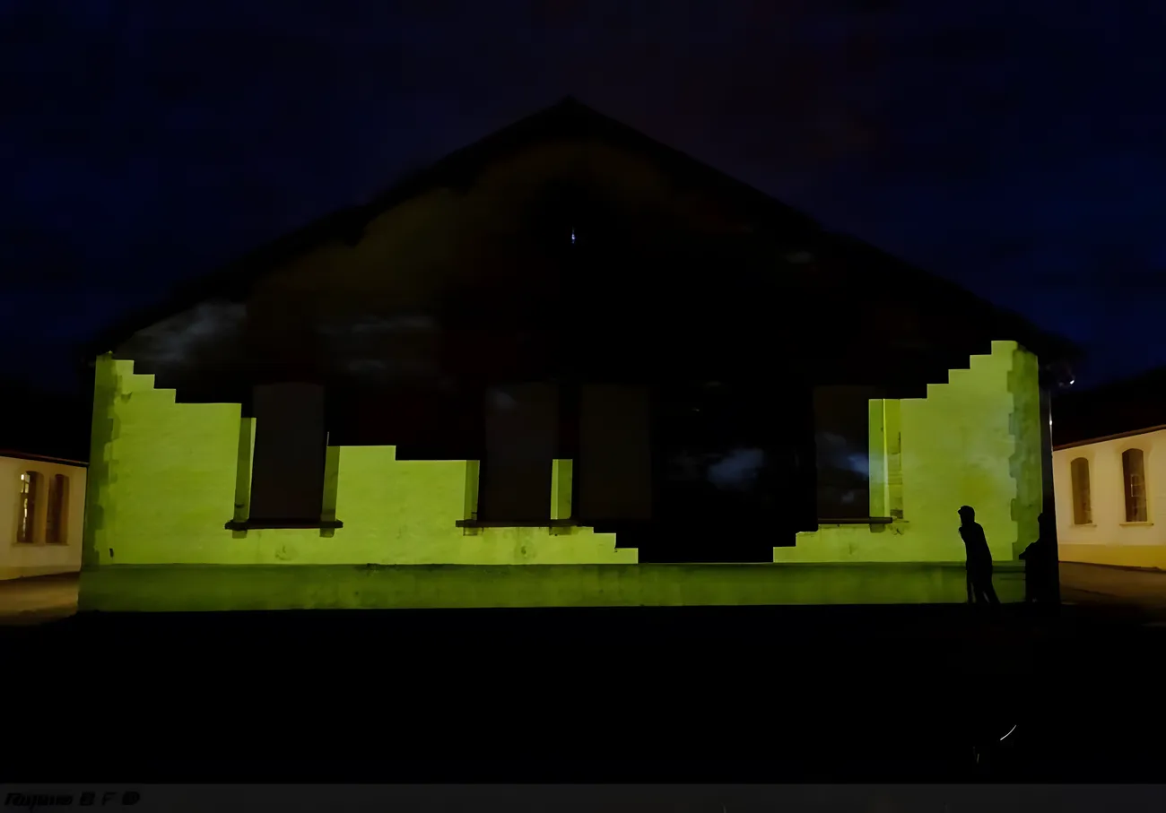 The barrack facade washed in projected light, a lone silhouette at its base