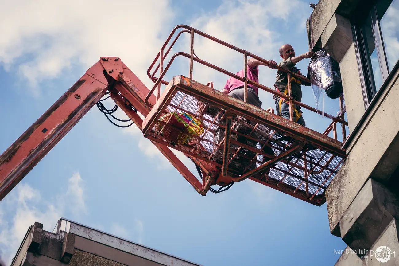 Daytime setup — the crew rigging lights from a cherry-picker high on a building facade