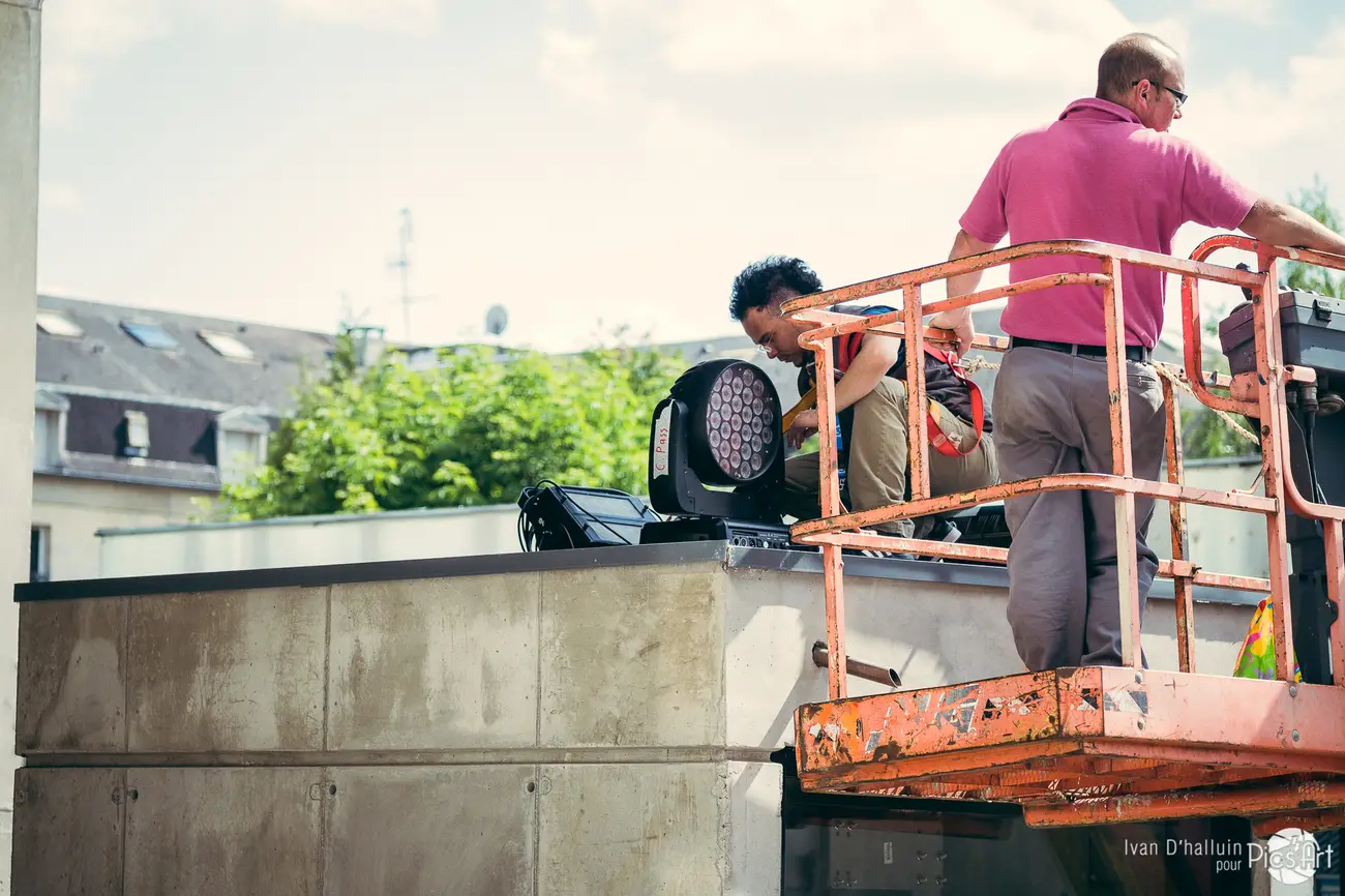 Daytime setup — installing a moving-head stage light on a rooftop, the town behind